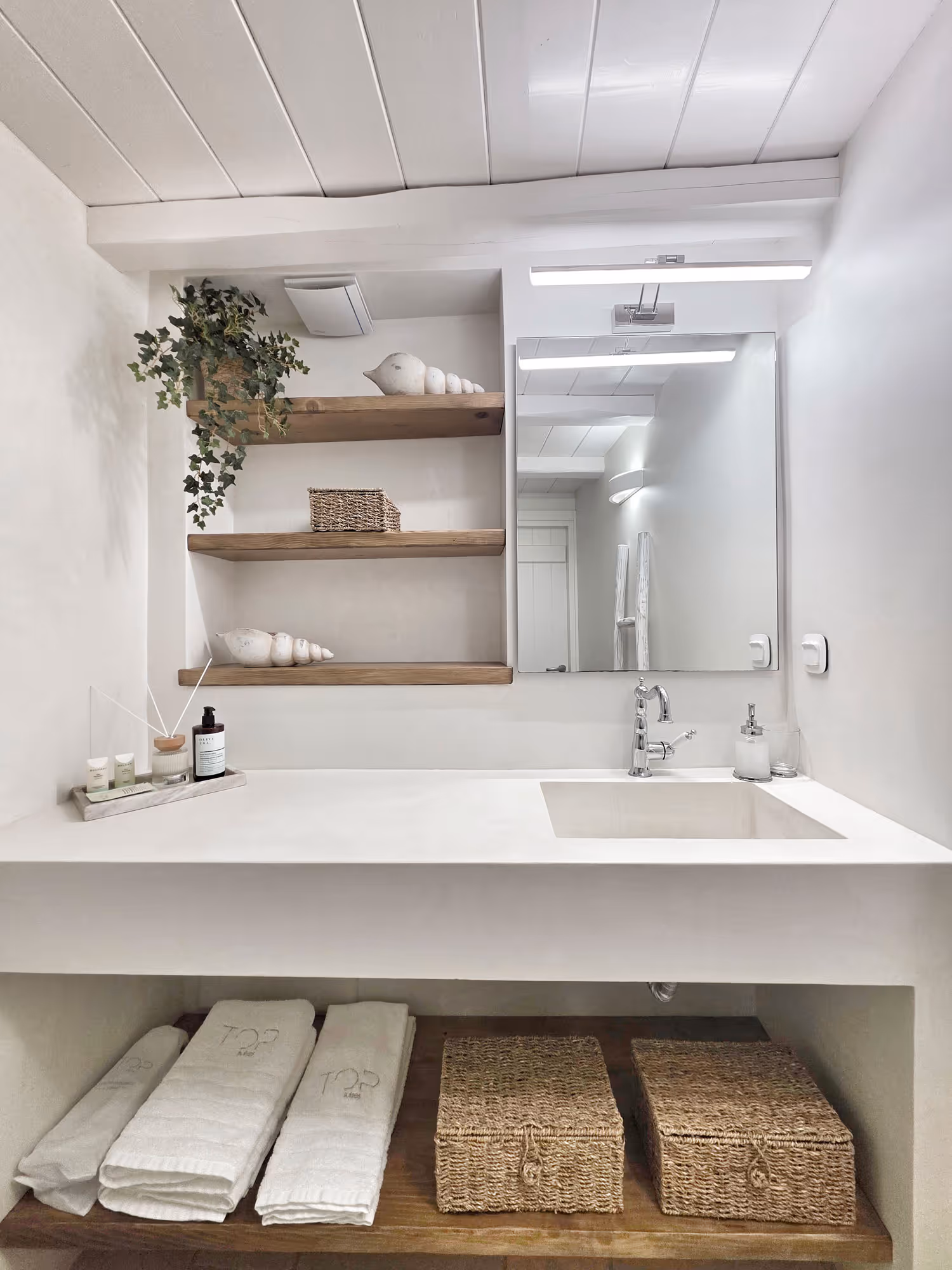Minimalist bathroom sink with wooden shelves, decorative birds, towels, and wicker baskets