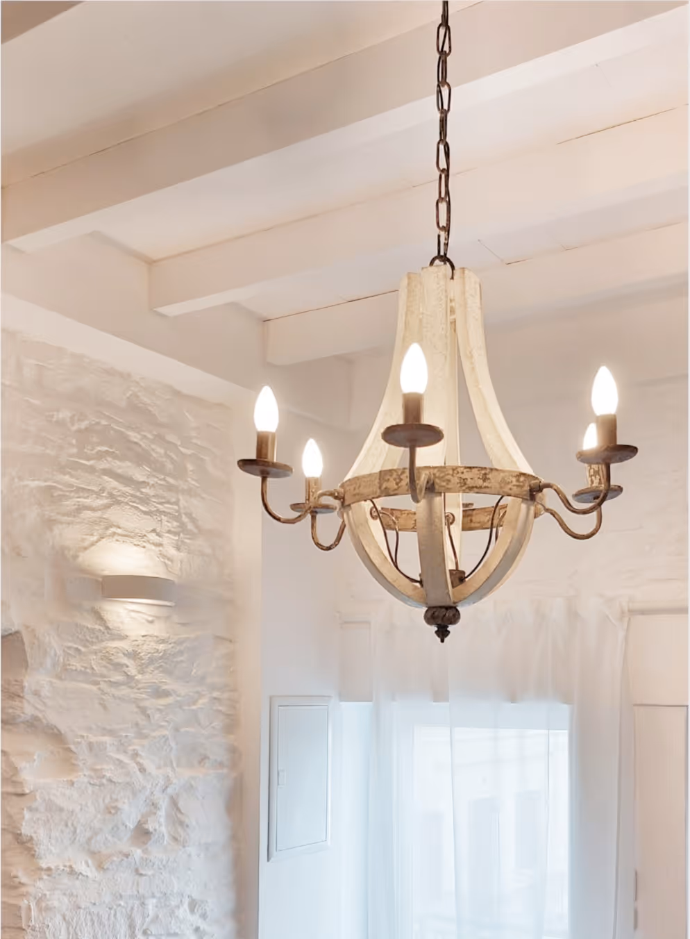 Rustic chandelier with five candle-shaped bulbs hanging from a white beamed ceiling.