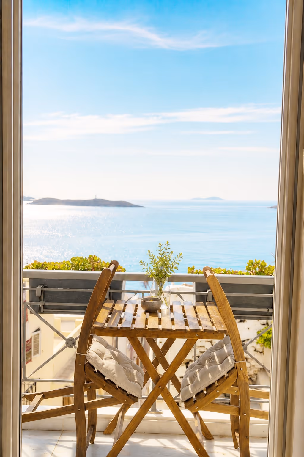 Wooden table and chairs with cushions on a balcony overlooking the sea and distant islands.