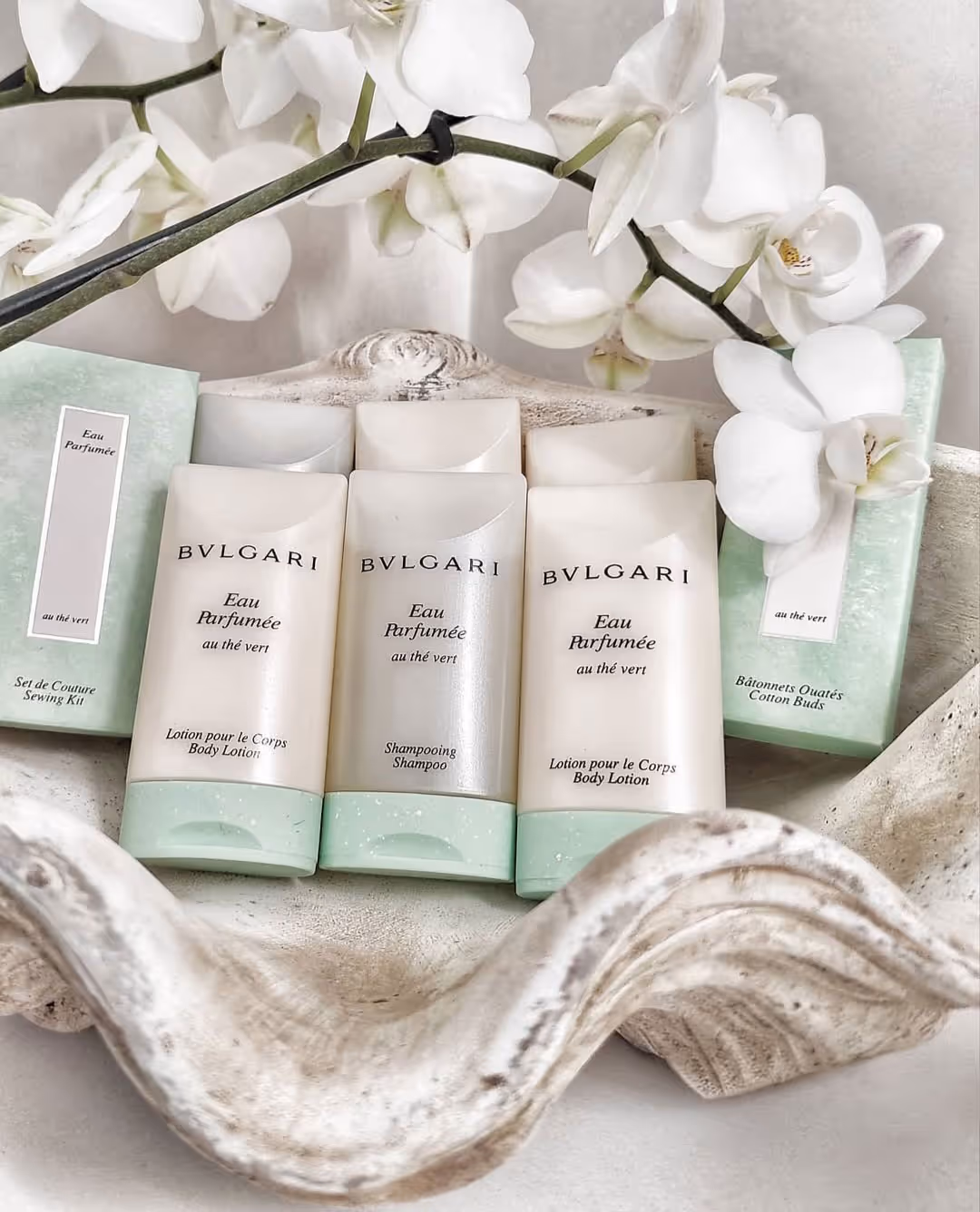 Bvlgari Eau Parfumée au thé vert toiletries with orchid flowers in a decorative shell dish.